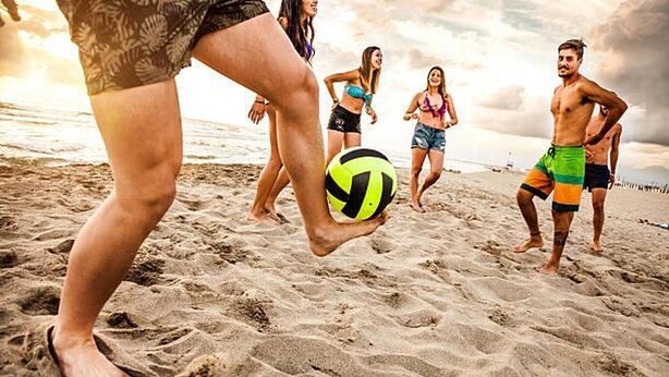 En strandvolleybollmatch där spelarna bär avslappnade strandkläder.