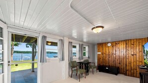 Une pièce avec vue sur un lac, un mur en bois, une table avec des chaises et un téléviseur.