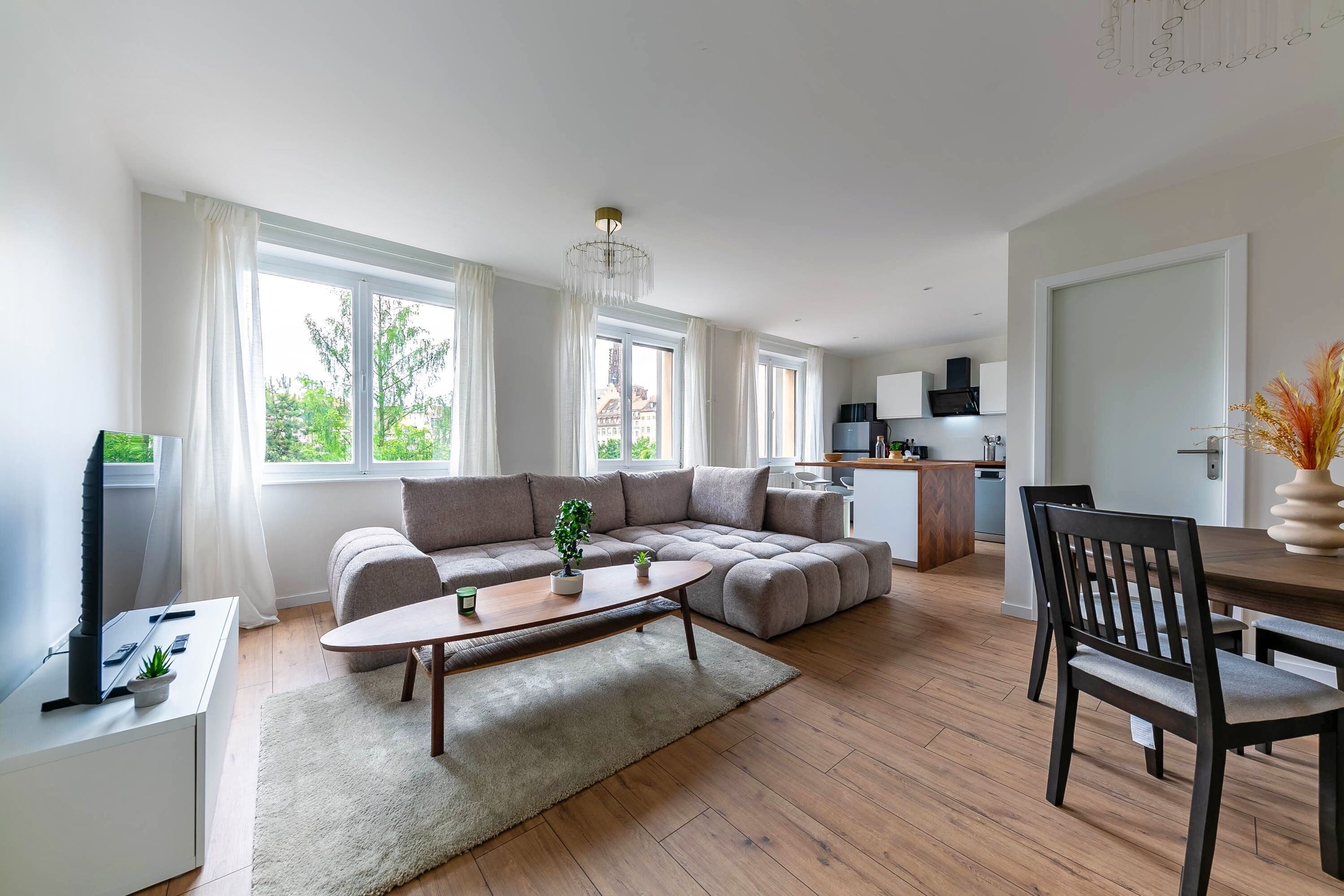 A modern living room with a sectional sofa, a dining table, and a kitchen area in the background.