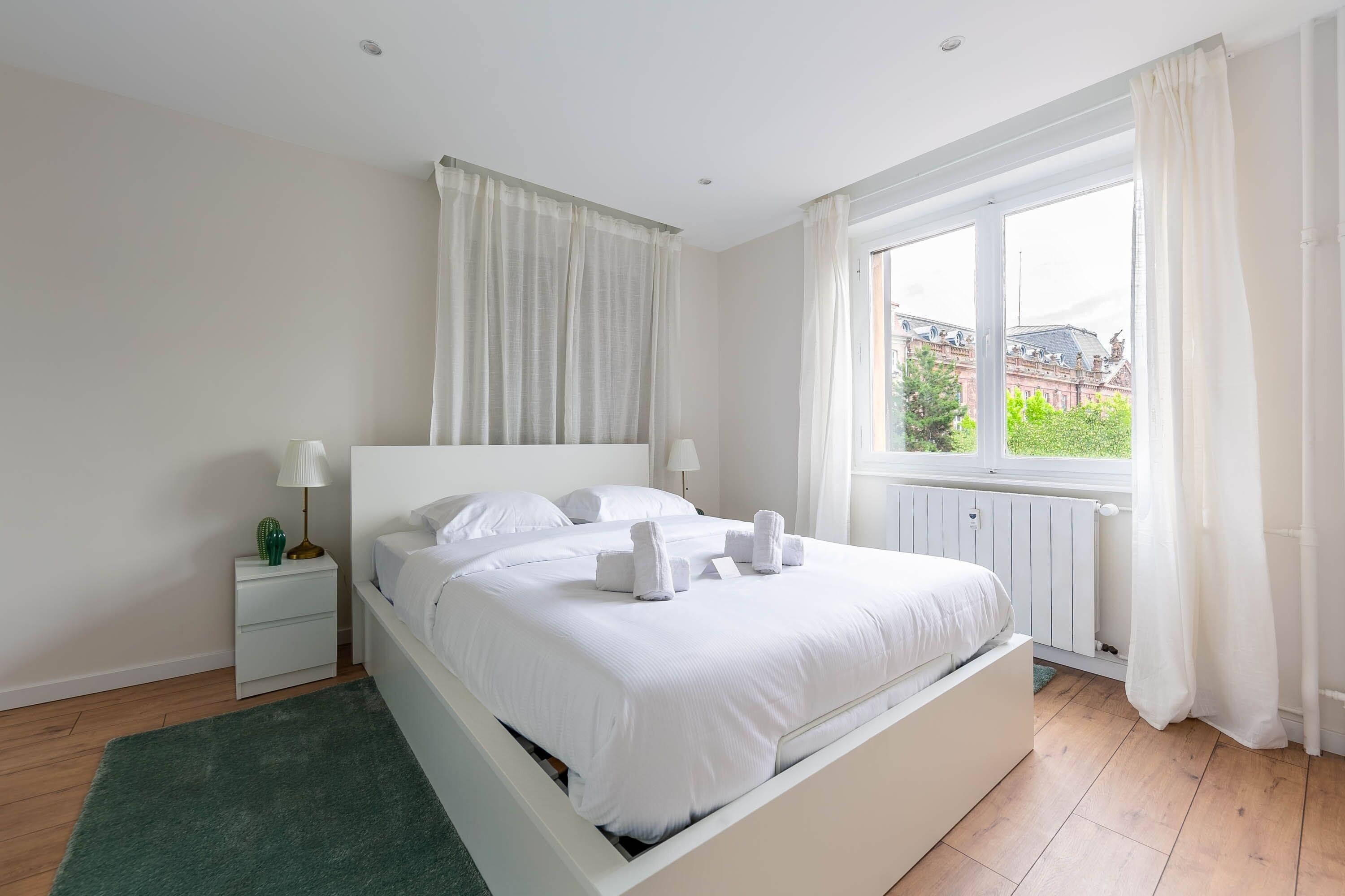 Une chambre bien rangée, avec un lit, des tables de chevet et une fenêtre avec des rideaux.
