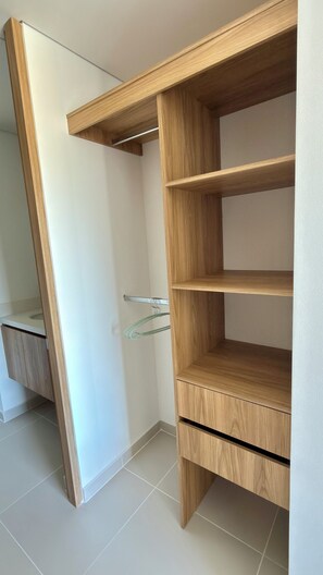 A wooden wardrobe with three shelves and a hanging rod, located in a room with white walls and tiled flooring. - Modern Premium Apartment on the Golden Mile, 11th Floor (ibague)