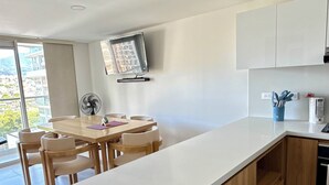 A modern kitchen with a central island, wooden cabinets, a dining area with chairs, and a view of buildings outside.