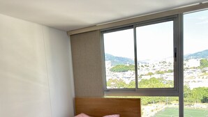 A bedroom with a large window, a bed, and a nightstand.