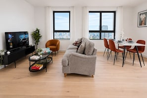 A modern living room with a sofa, dining table, chairs, a TV, and a city view. - Modern Greenwich flat with Balcony near The O2 & Canary Wharf (London)