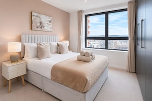 A modern bedroom with a large bed, bedside tables, a city view, and a painting on the wall. - Modern Greenwich flat with Balcony near The O2 & Canary Wharf (London)