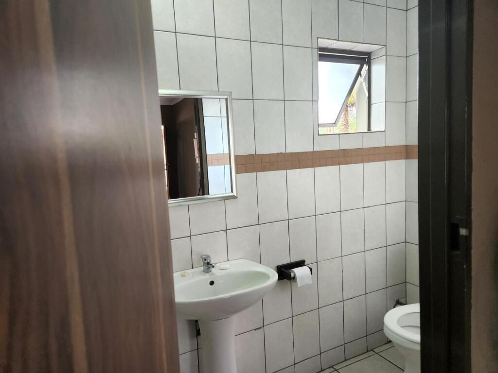 A bathroom with a white sink, a mirror, a toilet, and a small window.