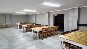Una sala de conferencias con varias mesas y sillas, piso de baldosas y una puerta al fondo.