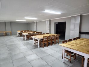 Una sala de conferencias con varias mesas y sillas, piso de baldosas y una puerta al fondo.
