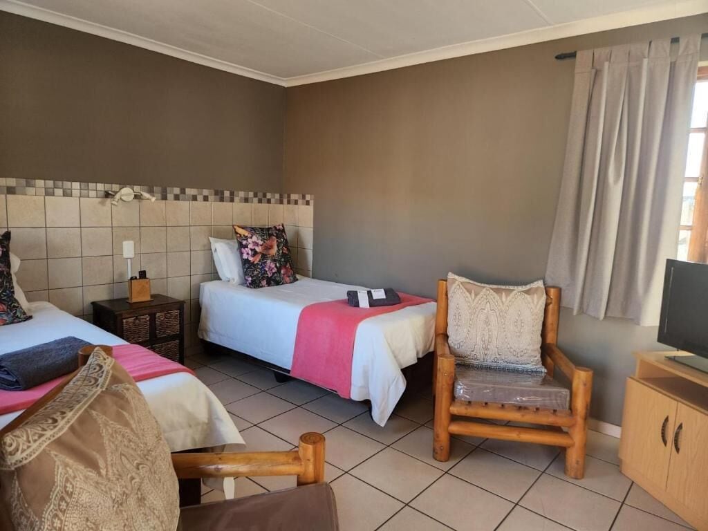 Quarto de hotel com duas camas, uma cadeira de madeira, uma televisão e um armário.