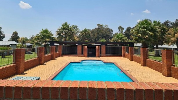 Ein rechteckiger Pool mit Mauerwerkrahmen, umgeben von einer Ziegelmauer und einem Metallzaun.