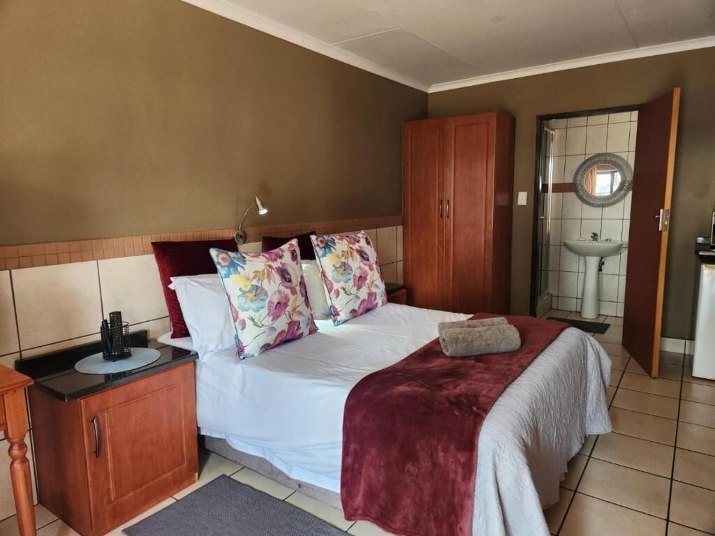 A bedroom with a bed, a wooden wardrobe, a bedside table, and a bathroom with a sink and mirror.