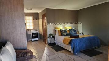 A bedroom with a bed, bedside table, and a small kitchenette.