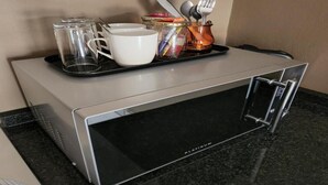 Una zona de cocina con un microondas, una bandeja con tazas, un tarro y utensilios.