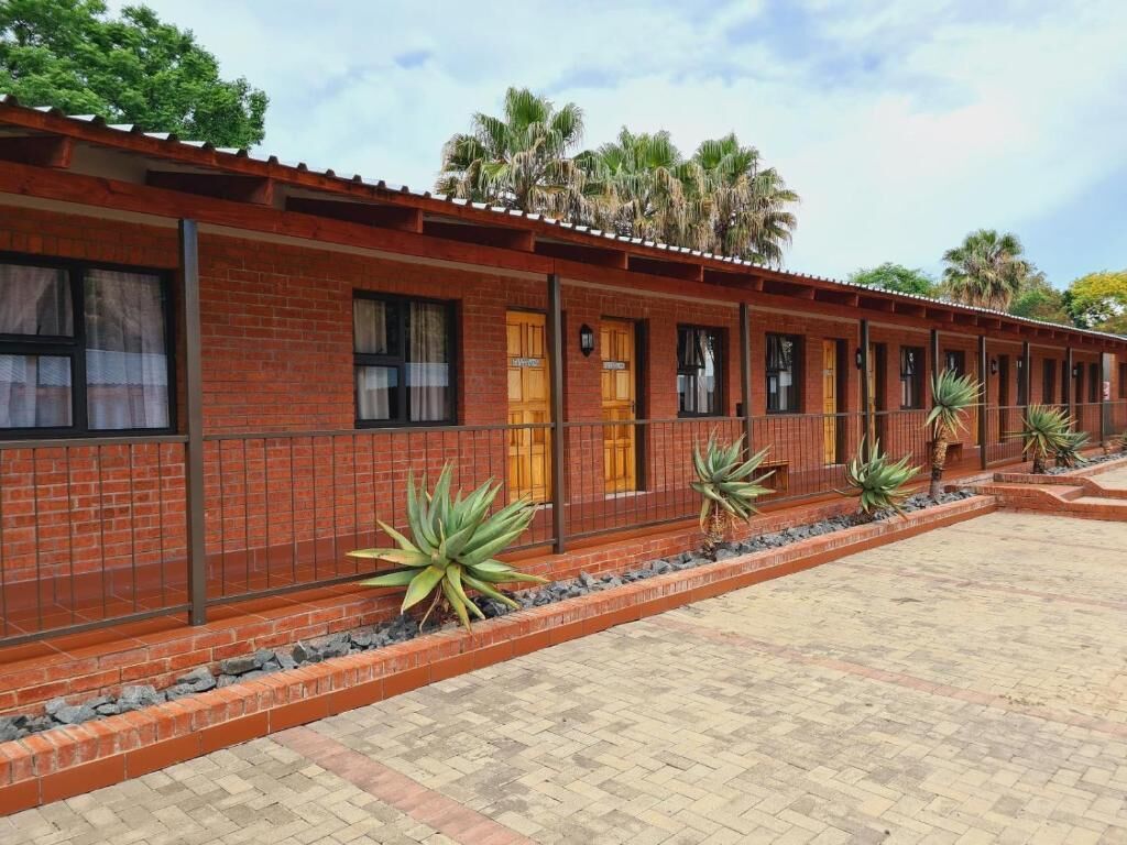 A brick building with multiple windows and doors, a paved walkway, and small plants along the walkway.