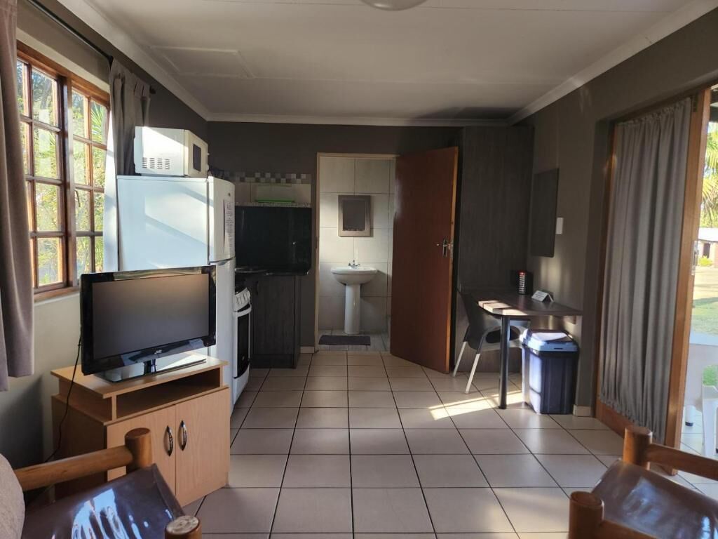 Une pièce équipée d’un téléviseur posé sur un meuble en bois, d’une kitchenette avec un réfrigérateur et un four à micro-ondes, d’un évier et d’un coin repas comprenant une table et des chaises.