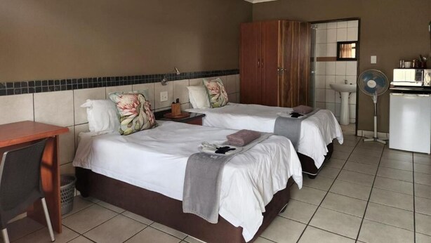 Habitación de hotel con dos camas, un escritorio, un armario y un baño visible a través de una puerta abierta.