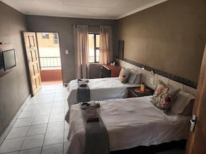 Een hotelkamer met twee bedden, een bureau, een televisie en uitzicht op buiten.