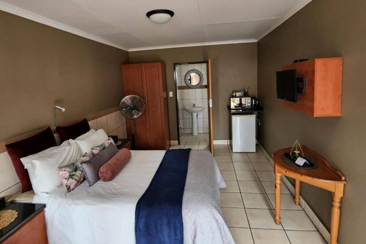 Habitación de hotel con cama, mesita de noche, una pequeña mesa de madera, televisor y un área de kitchenette.