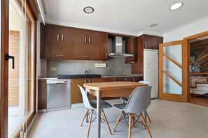 A modern kitchen with wooden cabinets, a stainless steel range hood, and a dining area with a wooden table and two chairs. - Disconnect in Galicia: A Journey to the Sea (Pontevedra)