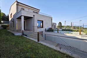 Uma casa moderna de dois andares com varanda, escadaria e vista para a água.