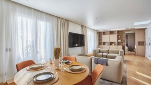 Un saló modern amb zona de menjador, un sofà i un televisor fixat a la paret.