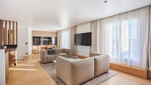 Un saló modern amb un sofà, una televisió de pantalla plana i una cuina al fons.