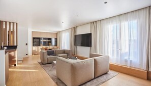 A modern living room with a sofa, a flat-screen TV, and a kitchen in the background. - A RARE COMBINATION OF LUXURY, COMFORT & PANORAMIC VIEWS OF THE EIFFEL TOWER (Paris)