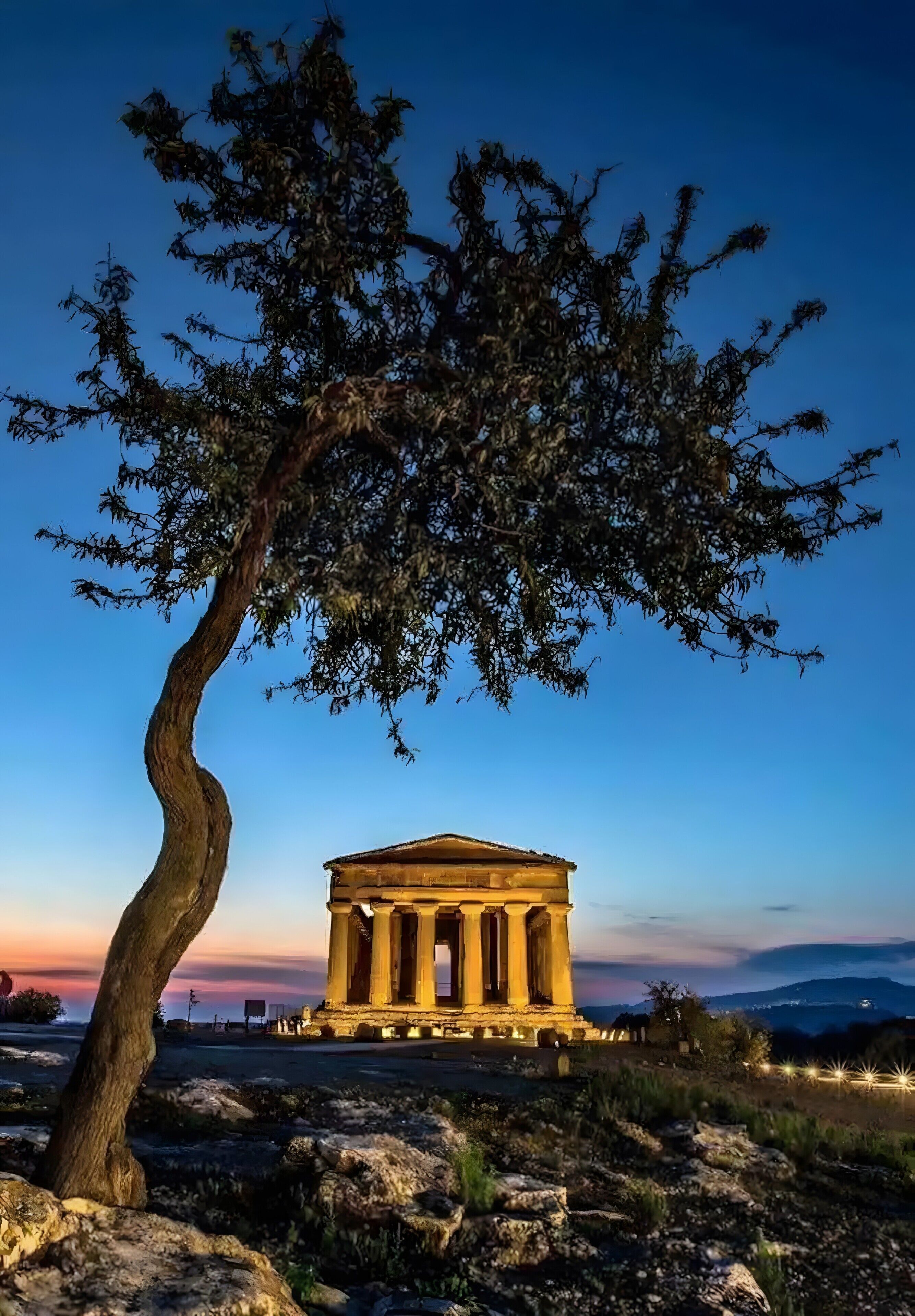 A classical building with columns, surrounded by rocks and a tree.