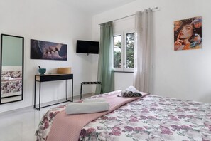 Un dormitorio con cama, escritorio, silla, televisor y ventana con cortinas.