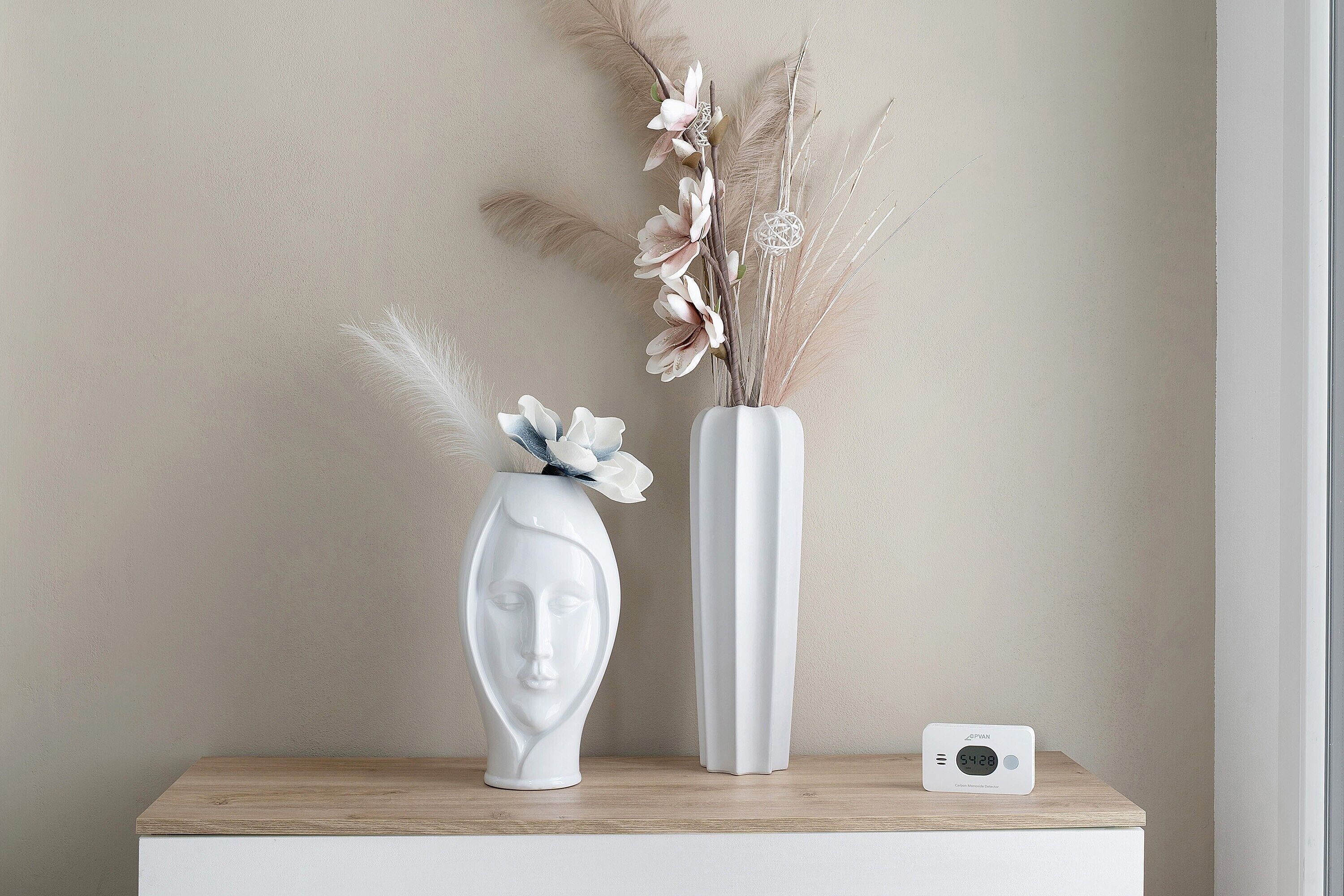 Un vase blanc contenant des fleurs séchées et un autre vase blanc avec une composition florale, le tout posé sur une surface en bois.