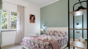 Un dormitorio con cama, ventana con cortinas, estante en la pared y un cuadro.