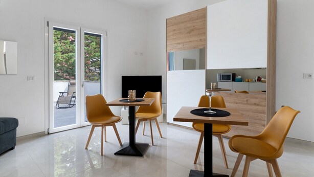 Un comedor moderno con un ventanal que da a un espacio exterior, un televisor de pantalla plana y un armario de madera.