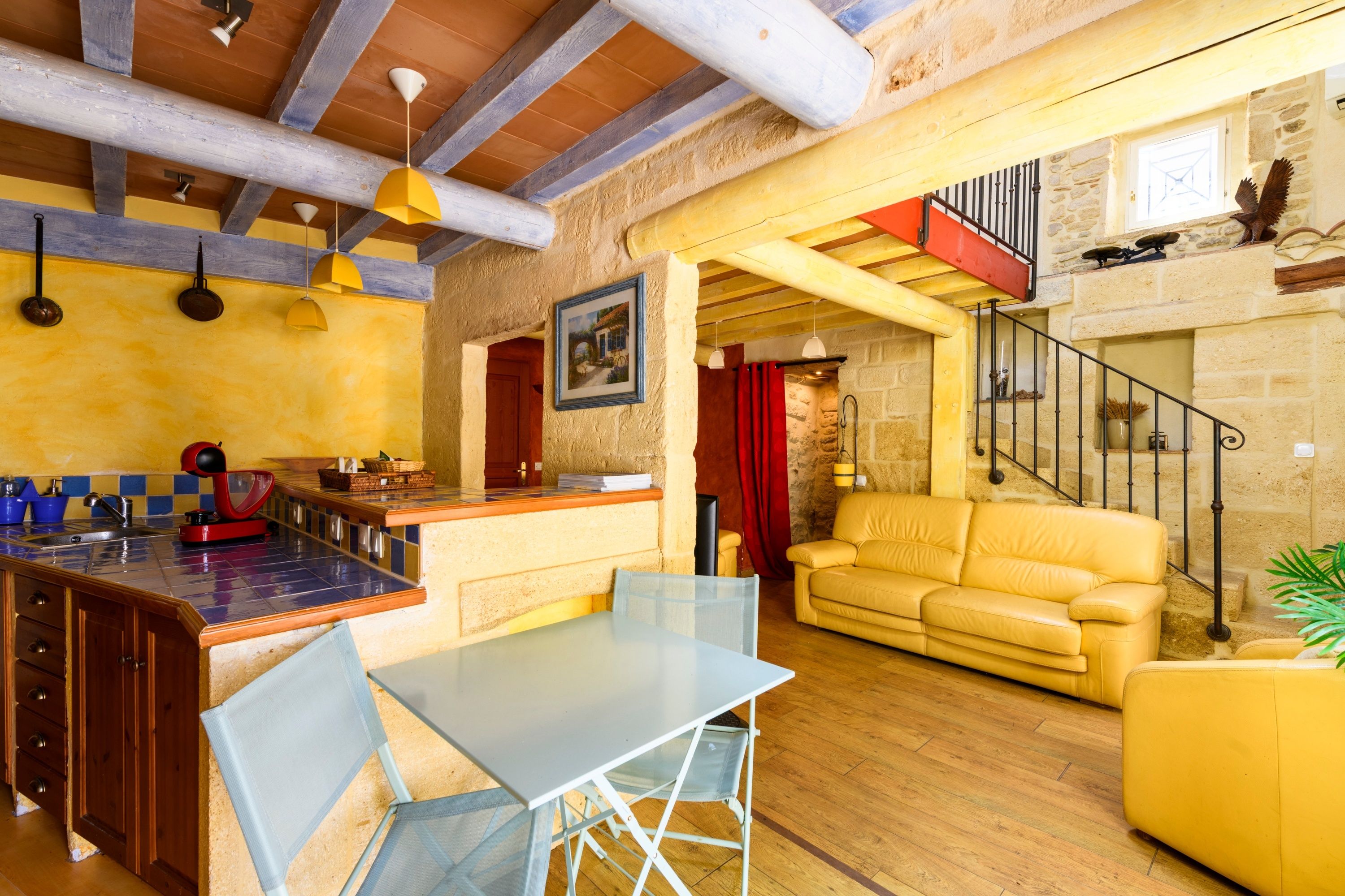 A spacious living area with a yellow sofa, a dining table with chairs, and a kitchen area with a red appliance.