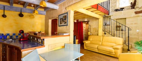 A spacious living area with a yellow sofa, a dining table with chairs, and a kitchen area with a red appliance.