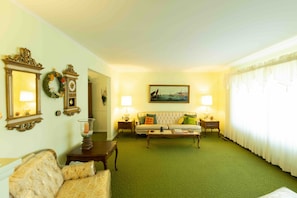 A living room with a green carpet, a sofa, a coffee table, two lamps, a painting, and a mirror. - Comfortable 4-Bedroom Home in Mt Morris (Mount Morris)
