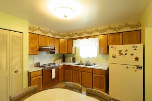 A kitchen with wooden cabinets, a refrigerator, a stove, and a dining table with chairs. - Comfortable 4-Bedroom Home in Mt Morris (Mount Morris)