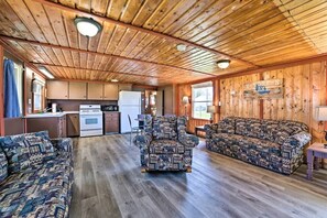 A cabin interior with a wooden ceiling, a kitchen area, a patterned sofa, and a dining table. - Waterfront Cabin with Kayaks, Dock & Fire Pit in Houghton Lake, Michigan (Houghton Lake)