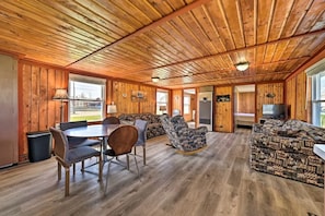 Una habitación amplia con paredes y techo de madera, un comedor con mesa y sillas, un sofá y un televisor.