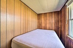 Une pièce aux murs lambrissés, avec un lit simple et une fenêtre.
