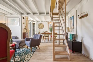 Ein Zimmer mit einer Holztreppe, einem Essbereich mit Tisch und Stühlen, einer Wanduhr und einem gerahmten Bild.