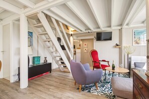 Ein modernes Wohnzimmer mit Treppe, einem roten Sessel, einem kleinen runden Tisch mit einer Flasche und einem an der Wand befestigten Fernseher.