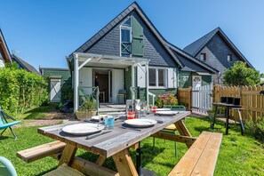 Ein Holzesitzgruppe mit Tisch, aufgebaut in einem Garten mit einem Haus im Hintergrund.