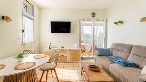 A modern living room with a sofa, dining table, and TV. - L’Échappée Océane - 100 m de la plage (Soulac-sur-Mer)
