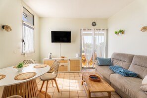 A modern living room with a sofa, dining table, and TV. - L’Échappée Océane - 100 m de la plage (Soulac-sur-Mer)