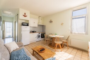 A compact living space with a kitchenette, dining area, and seating. - L’Échappée Océane - 100 m de la plage (Soulac-sur-Mer)