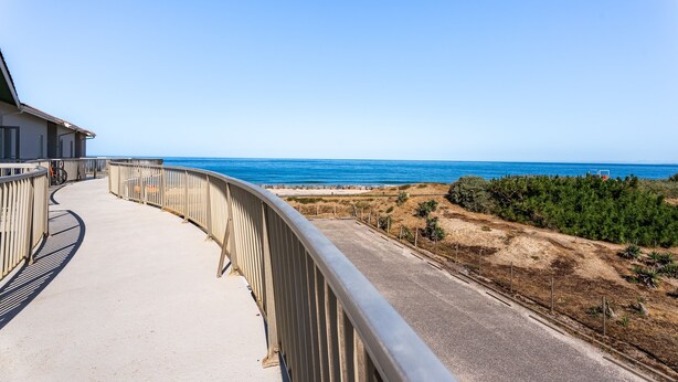 A coastal road with a metal railing, a clear blue sky, and the ocean in the distance. - L’Échappée Océane - 100 m de la plage (Soulac-sur-Mer)