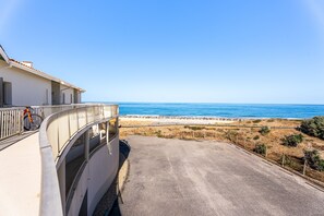 A coastal road leading to a beach with a white building on the left. - L’Échappée Océane - 100 m de la plage (Soulac-sur-Mer)