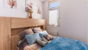 A bedroom with a wooden headboard, a bed with plaid bedding, and wall art. - L’Échappée Océane - 100 m de la plage (Soulac-sur-Mer)