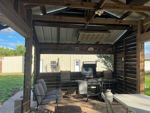 Un espacio al aire libre techado con una parrilla, asientos y un tanque de gas.