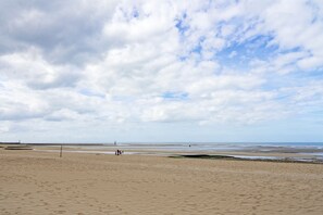 A wide sandy beach with a few people walking, a distant pier, and a cloudy sky. - La Réglisse - À moins d’1 km de la plage (Courseulles-sur-Mer)